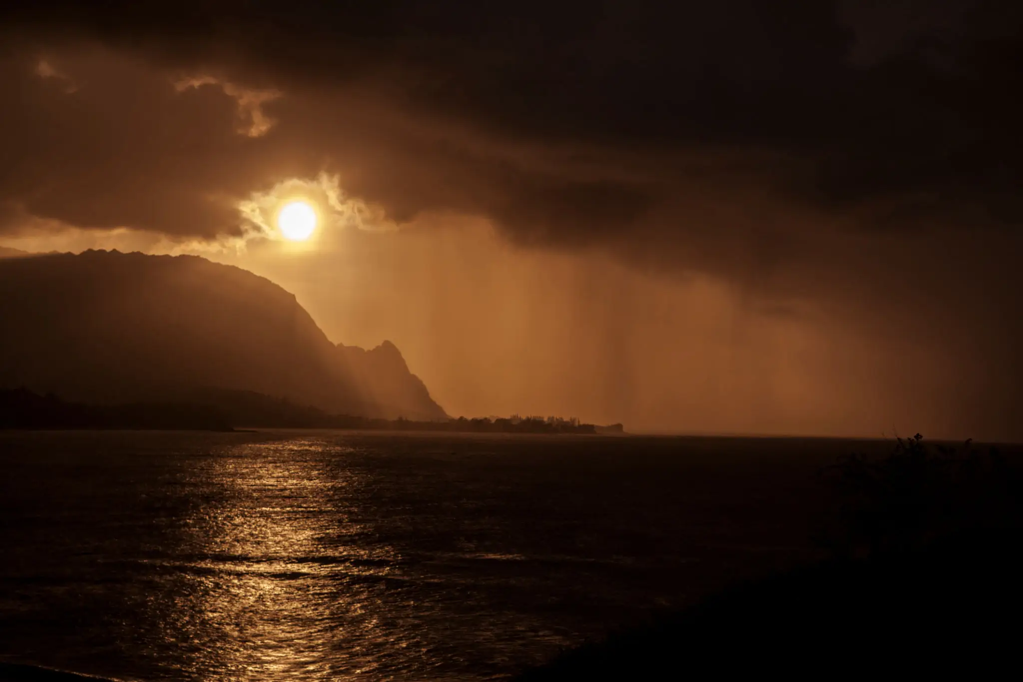 Sunset over a misty ocean with dark clouds and silhouetted mountains.