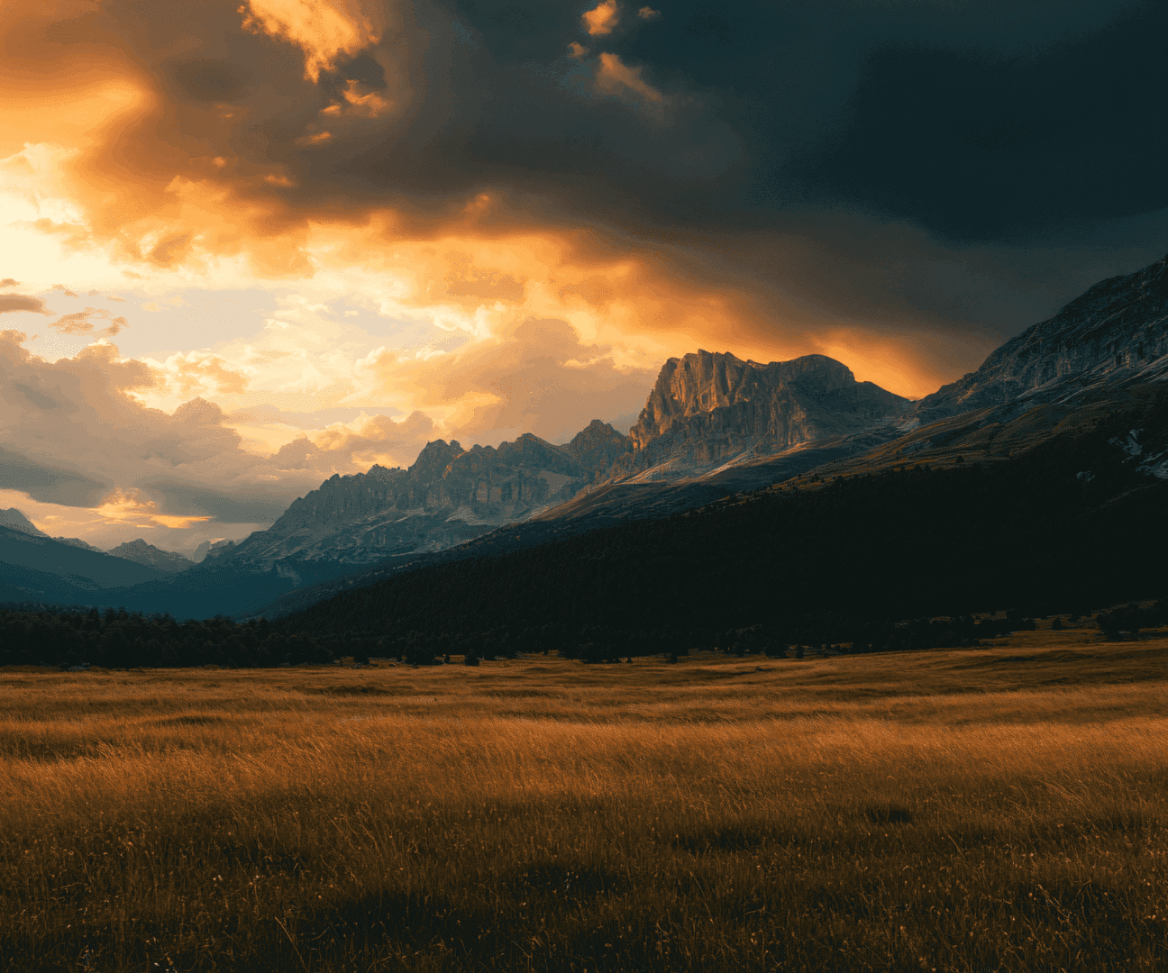 Sunset over a vast field with dramatic mountain clouds.