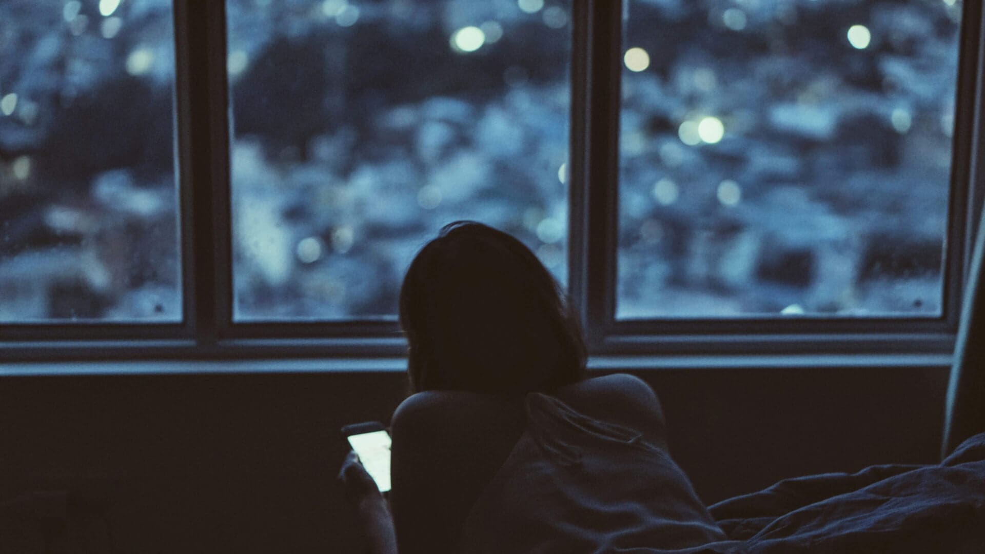 Silhouette of a person looking out a window at dusk.