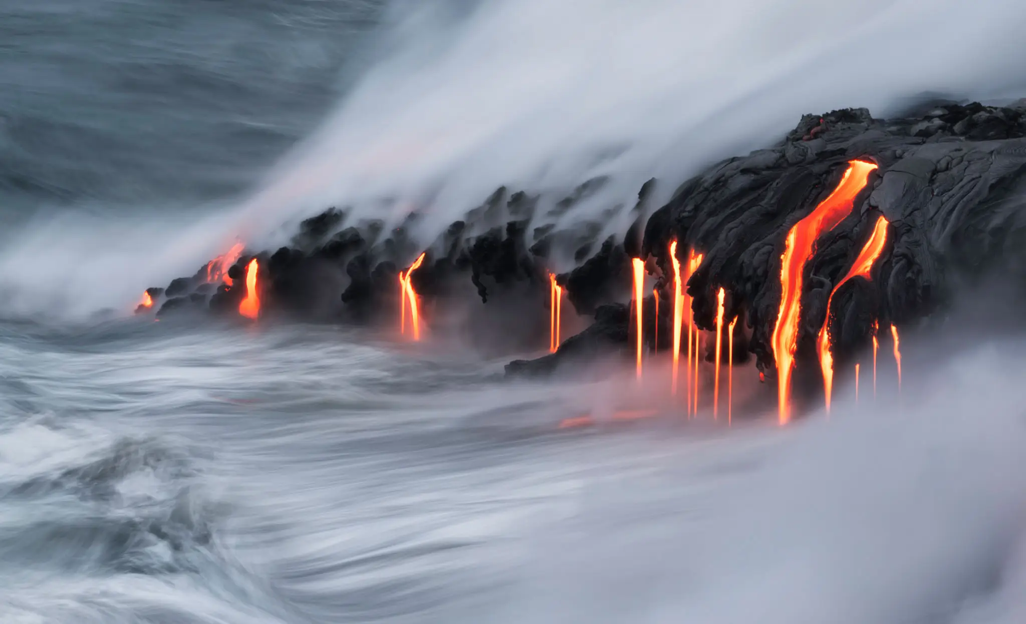 Lava flows into the ocean, creating steam and glowing streams.
