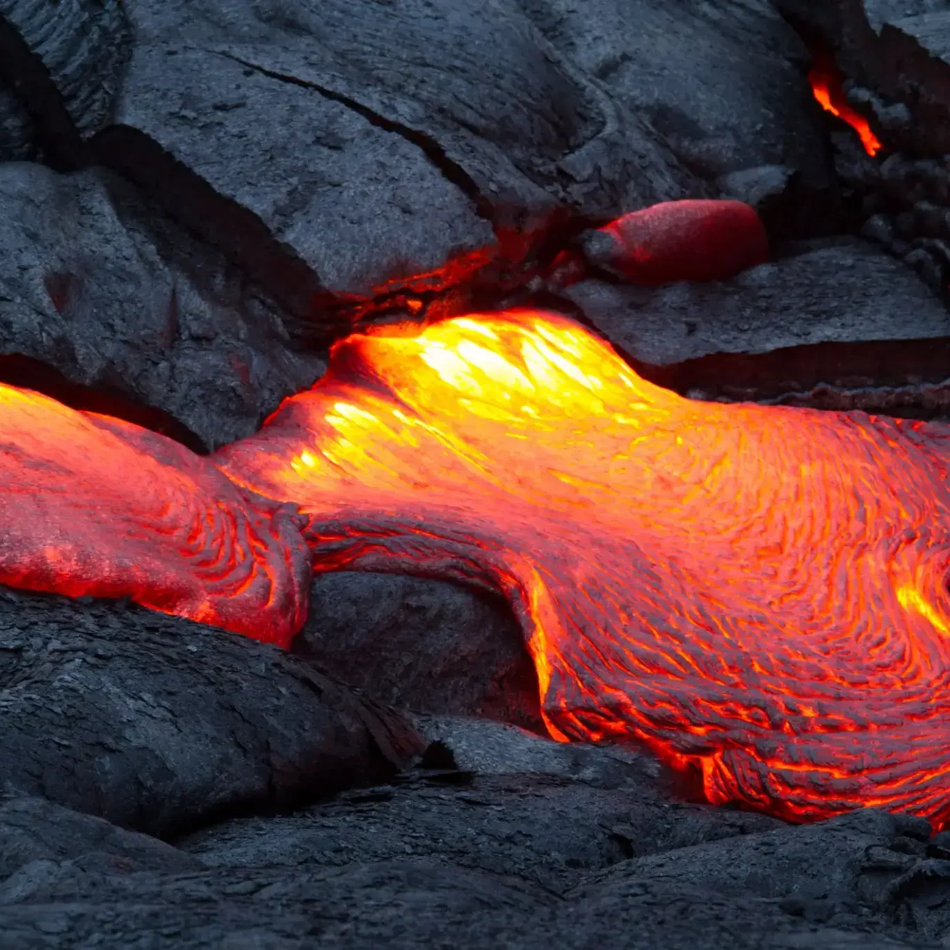 Bright orange lava flowing over dark volcanic rock.